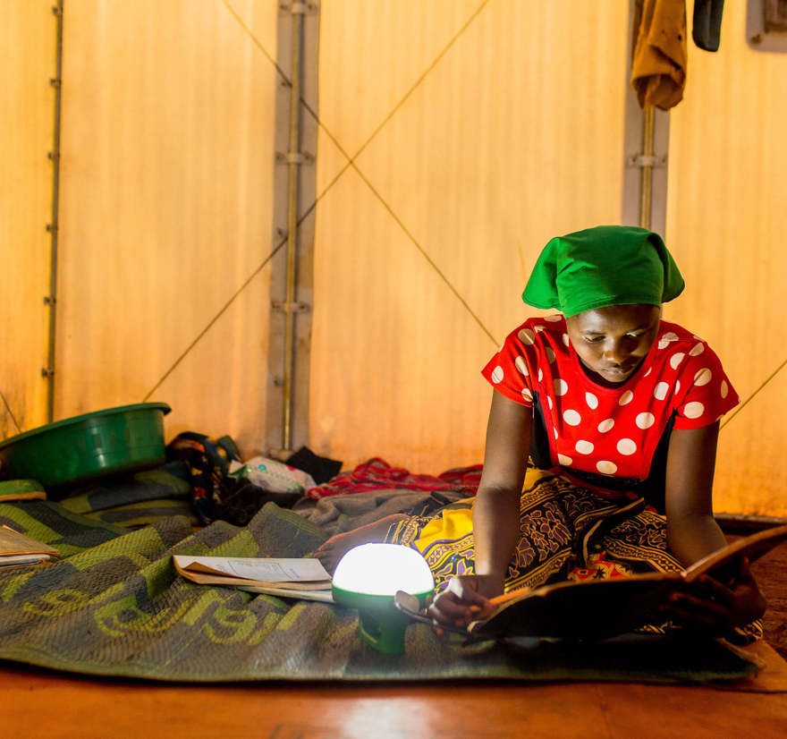 A refugee woman in Tanzania studies by lamplight.
