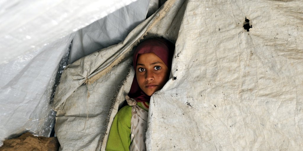 Lujain Qasim, 11, looks through an opening in her family's tent at the Dharawan settlement