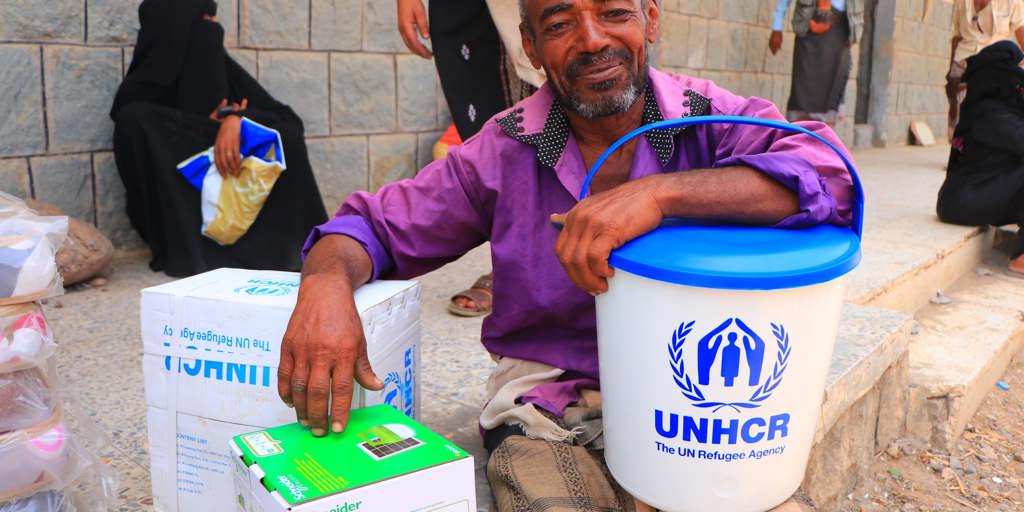 Man with UNHCR supplies looks at camera. Displaced families in Yemen receive essential household items.