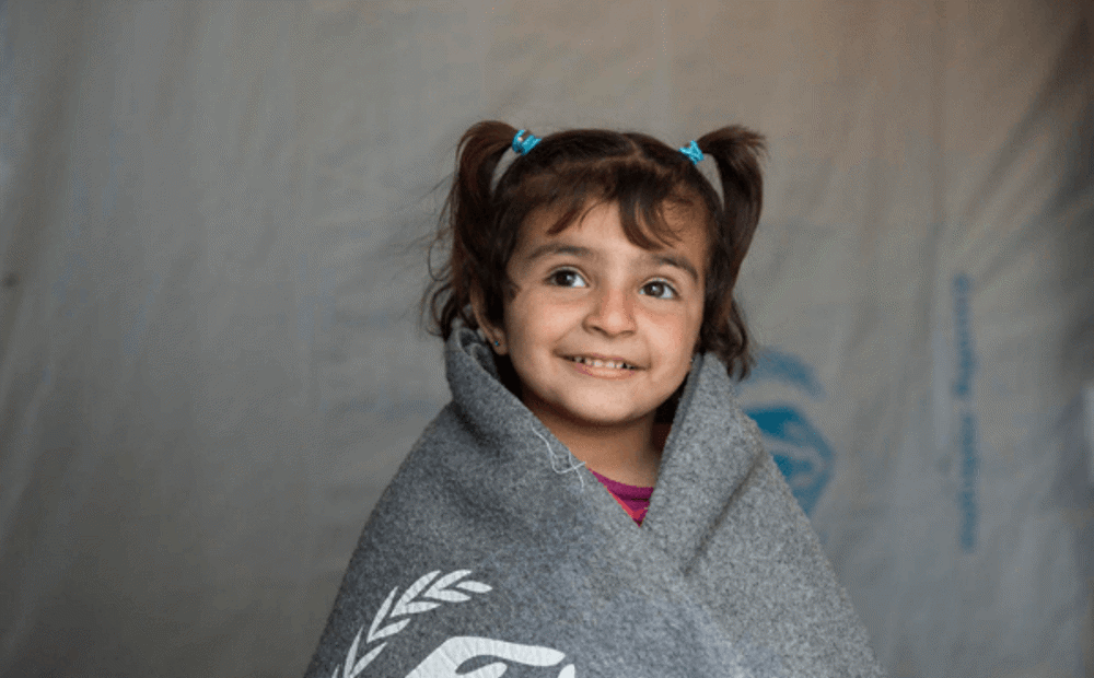 Small refugee child huddles under warm UNHCR blanket 