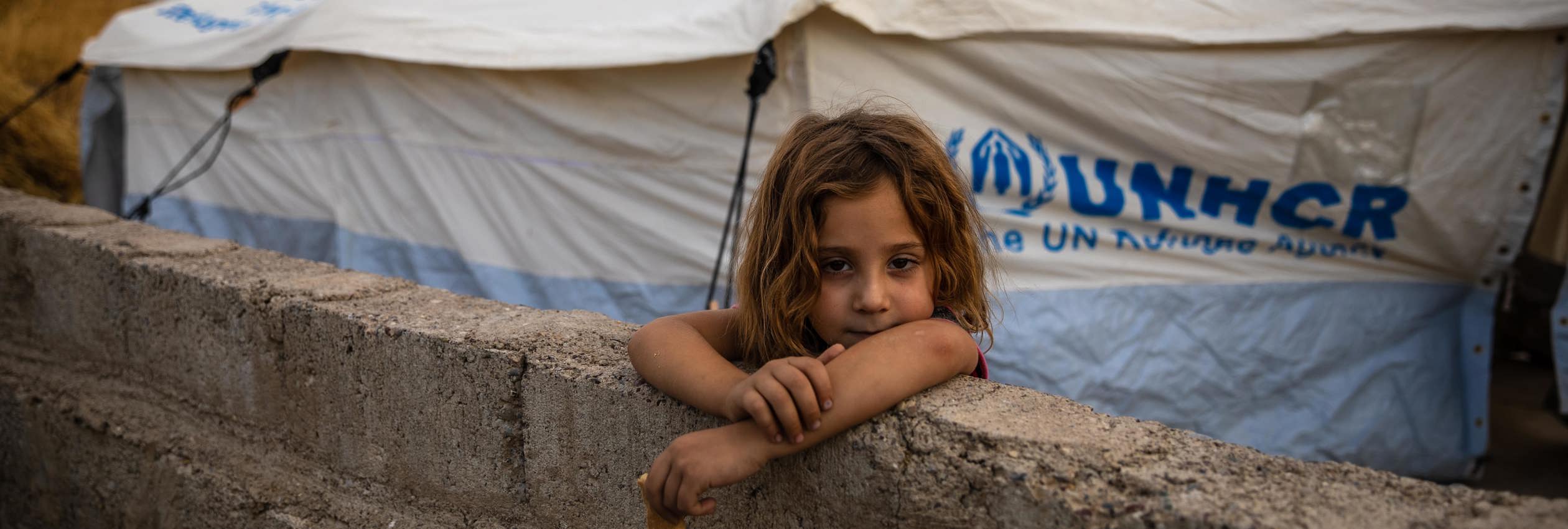 Eight-year-old Raghda Abbas Suleiman looks over a wall near her shelter at Bardarash camp in Duhok, Iraq, a day after arriving with her family.