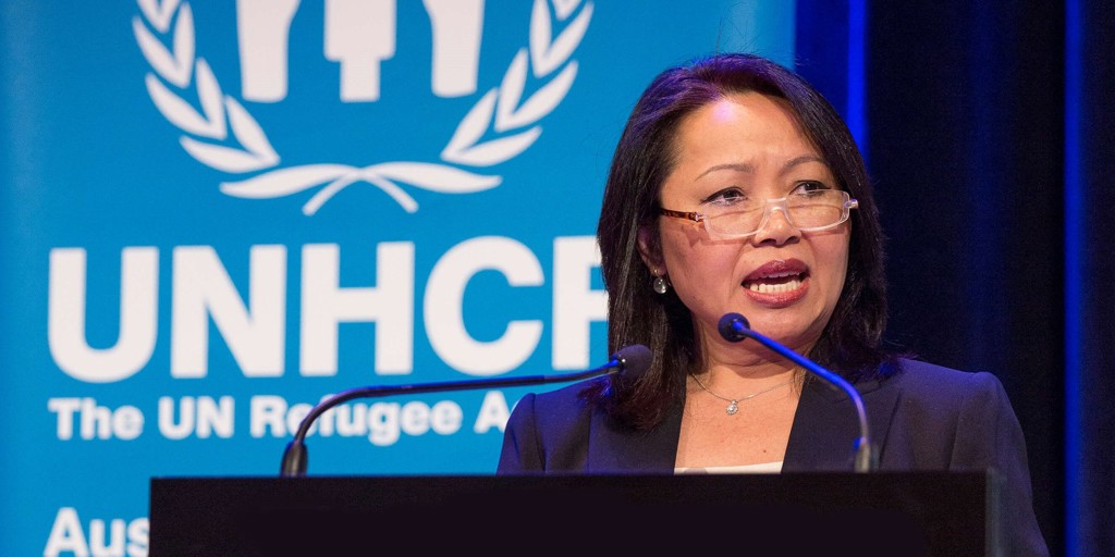 Special Representative Carina Hoang speaking behind a podium in front of Australia for UNHCR banner